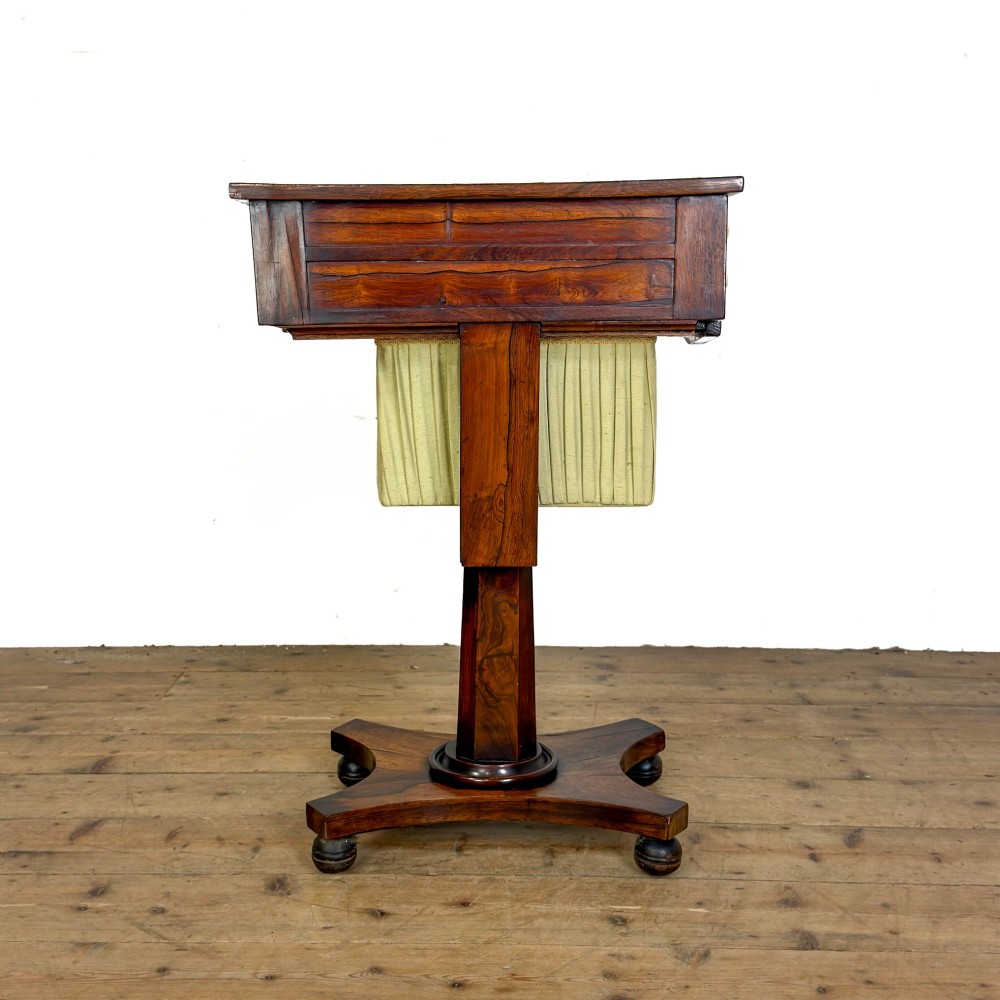 A 19th-century rosewood work table featuring small drawers, a pleated cream fabric basket underneath, a central pedestal support, and a quadruped base. View IX