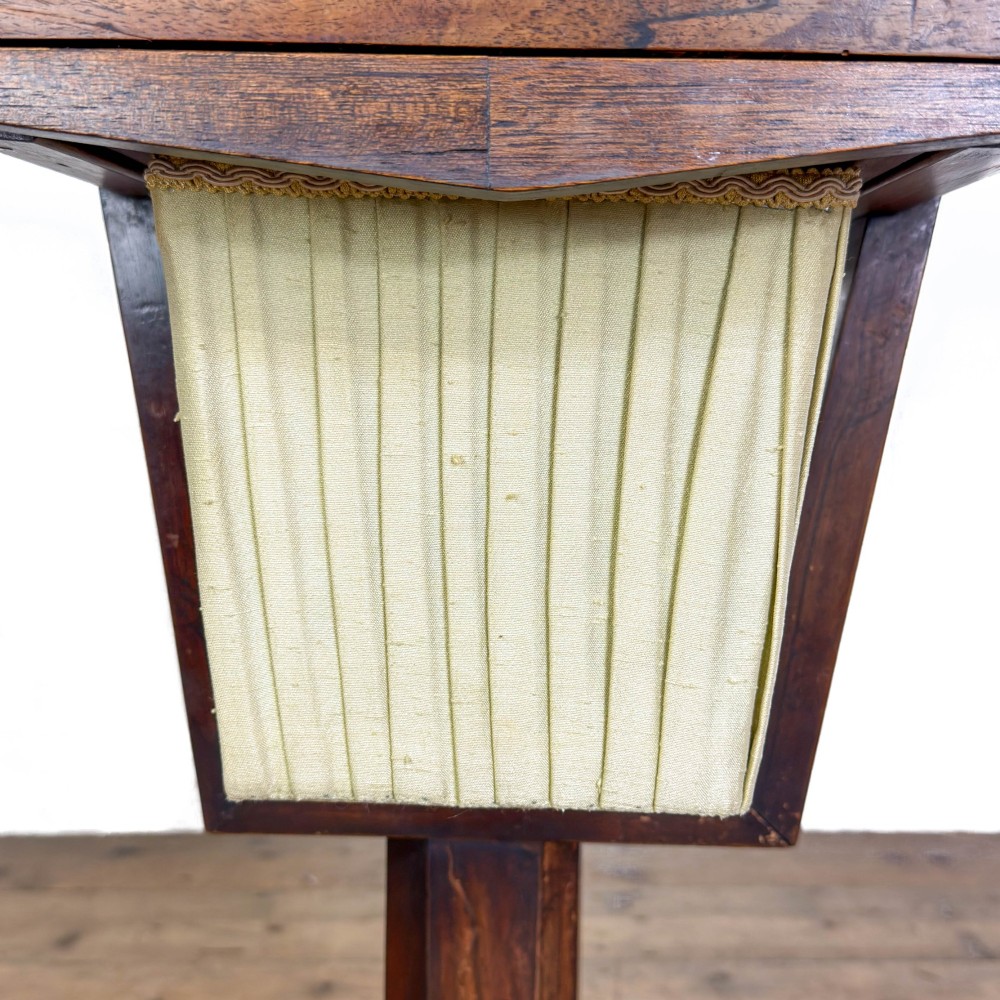 A 19th-century rosewood work table featuring small drawers, a pleated cream fabric basket underneath, a central pedestal support, and a quadruped base. View XI