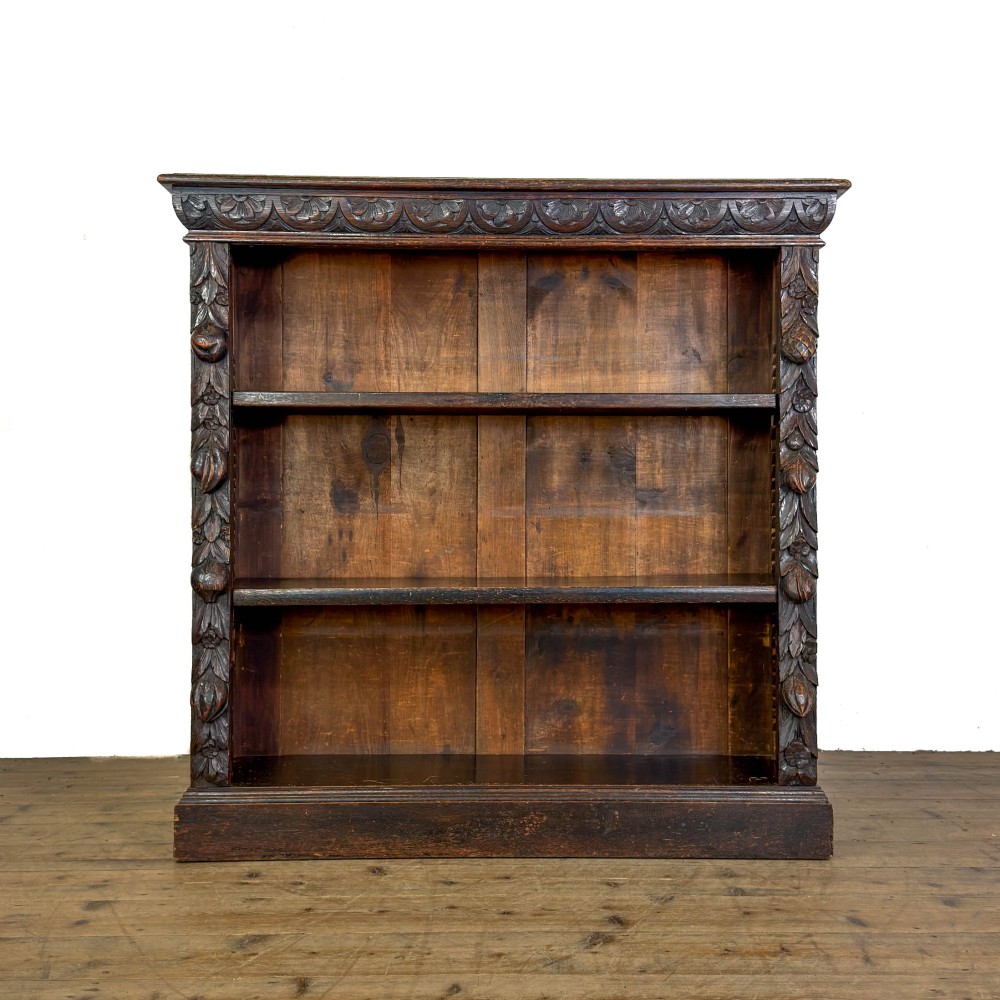 An antique dark oak open bookcase featuring hand-carved foliate detailing along the stiles and a carved upper frieze.