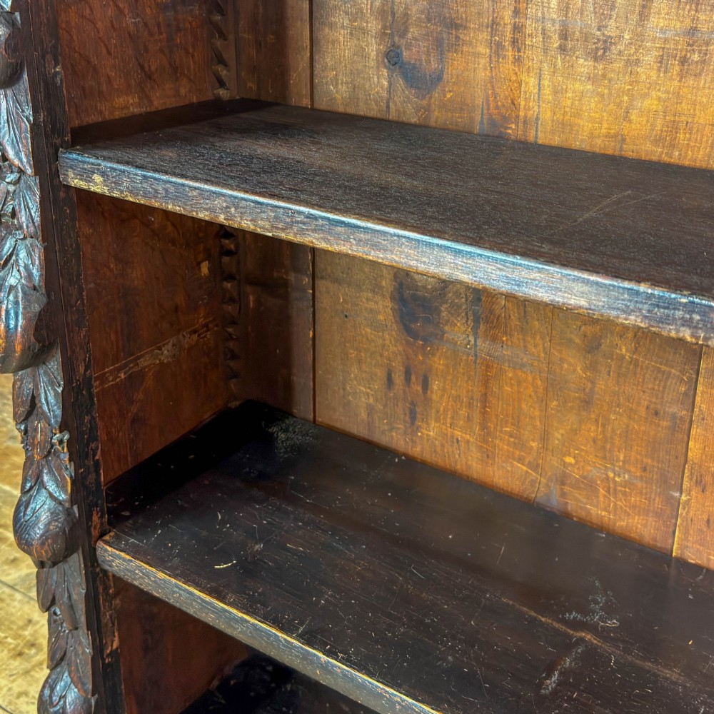 An antique dark oak open bookcase featuring hand-carved foliate detailing along the stiles and a carved upper frieze. View II