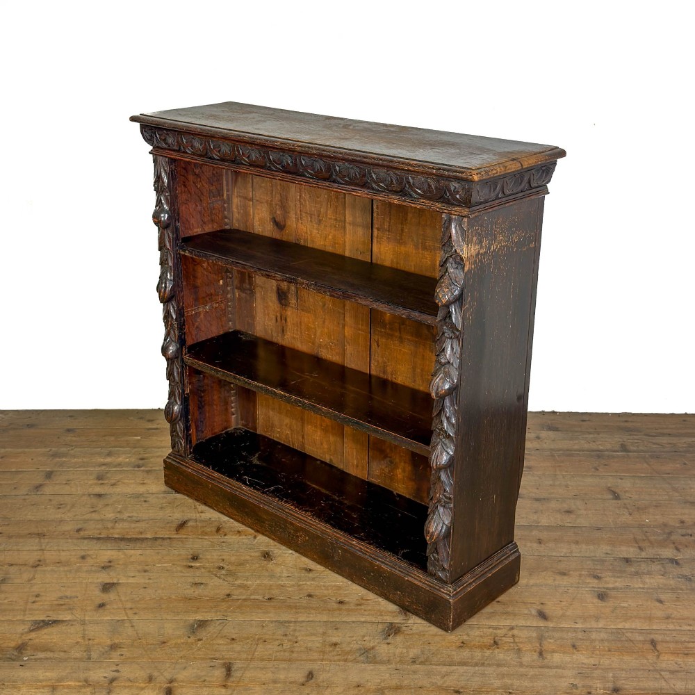 An antique dark oak open bookcase featuring hand-carved foliate detailing along the stiles and a carved upper frieze. View III