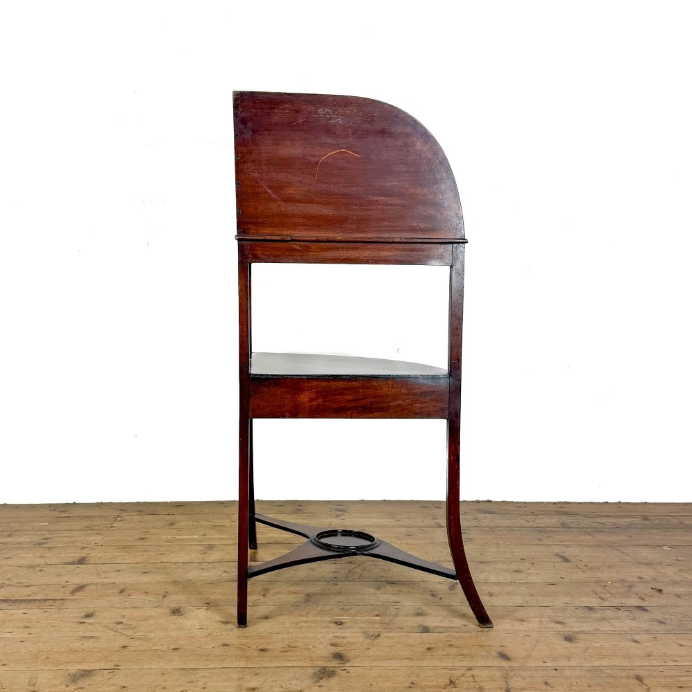 An antique mahogany corner washstand featuring a curved splashback, top circular basin cut-outs, a central drawer, and splayed legs connected by a lower stretcher shelf. View II