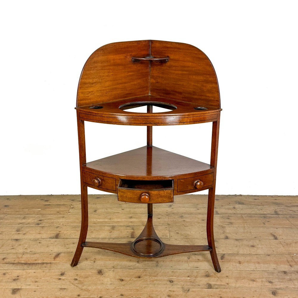 An antique mahogany corner washstand featuring a curved splashback, top circular basin cut-outs, a central drawer, and splayed legs connected by a lower stretcher shelf. View IV