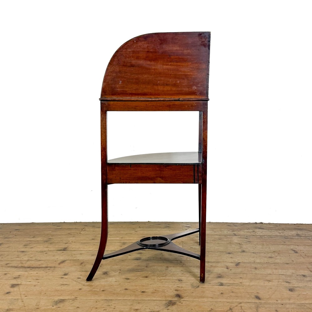 An antique mahogany corner washstand featuring a curved splashback, top circular basin cut-outs, a central drawer, and splayed legs connected by a lower stretcher shelf. View VI