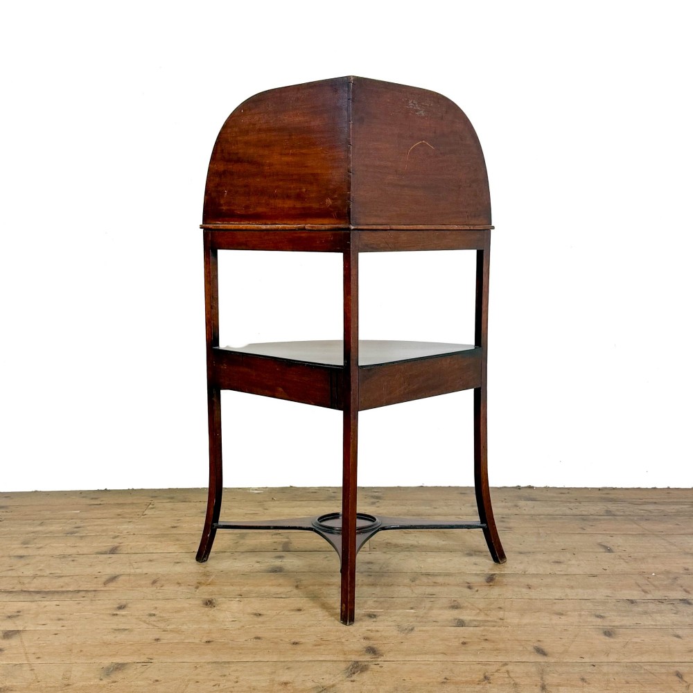An antique mahogany corner washstand featuring a curved splashback, top circular basin cut-outs, a central drawer, and splayed legs connected by a lower stretcher shelf. View VII