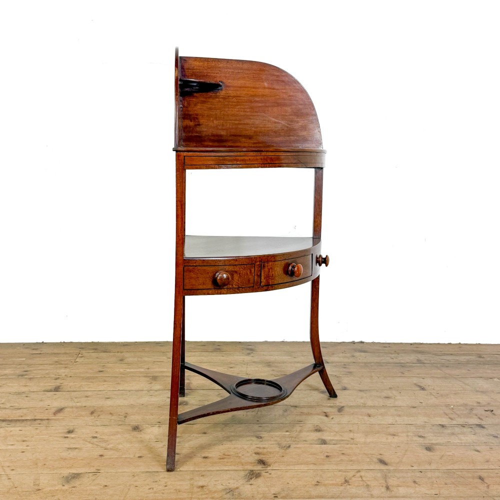 An antique mahogany corner washstand featuring a curved splashback, top circular basin cut-outs, a central drawer, and splayed legs connected by a lower stretcher shelf. View VIII