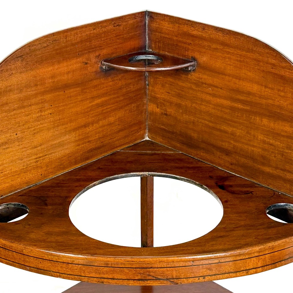 An antique mahogany corner washstand featuring a curved splashback, top circular basin cut-outs, a central drawer, and splayed legs connected by a lower stretcher shelf. View X