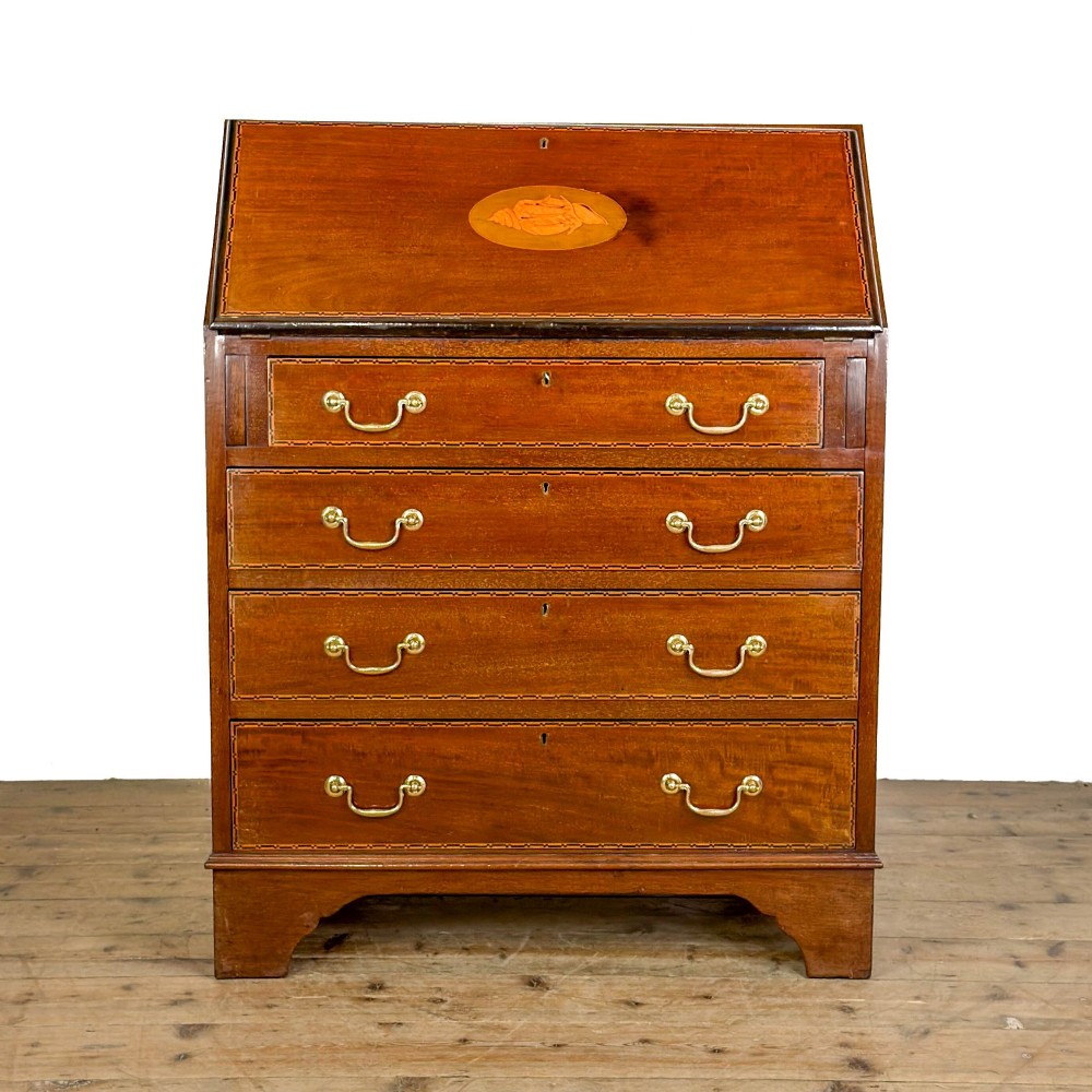 An antique Edwardian mahogany writing bureau featuring a sloping fall-front top with a shell marquetry inlay, situated above four graduating drawers with brass handles on bracket feet.