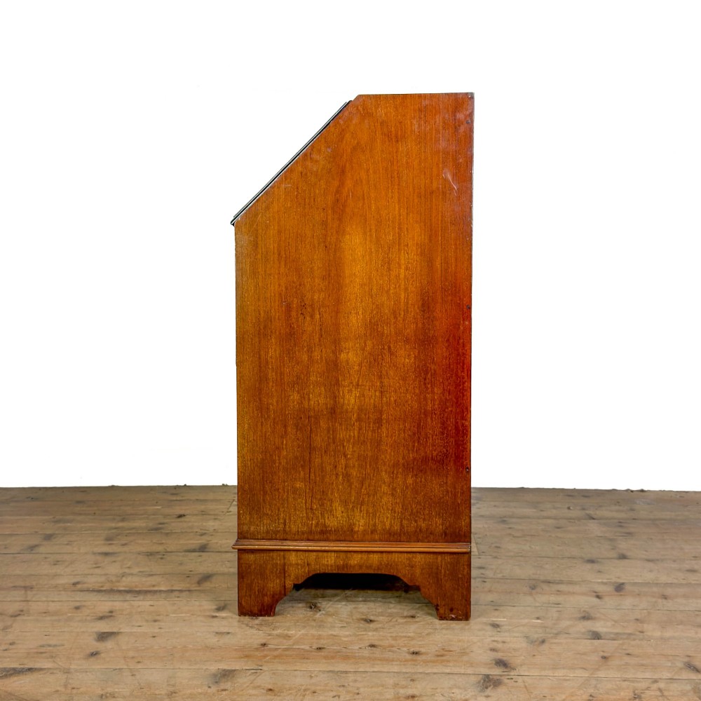 An antique Edwardian mahogany writing bureau featuring a sloping fall-front top with a shell marquetry inlay, situated above four graduating drawers with brass handles on bracket feet. View VI