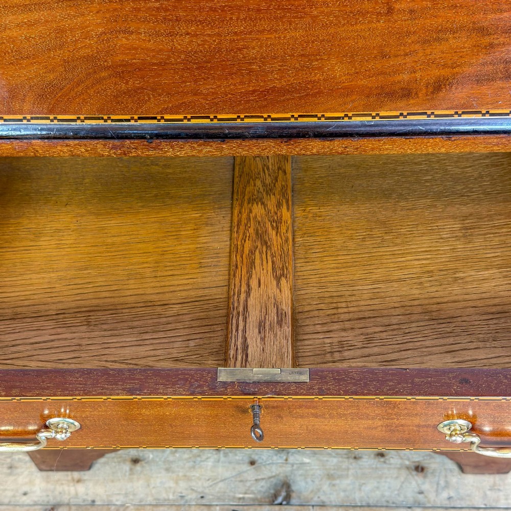 An antique Edwardian mahogany writing bureau featuring a sloping fall-front top with a shell marquetry inlay, situated above four graduating drawers with brass handles on bracket feet. View X