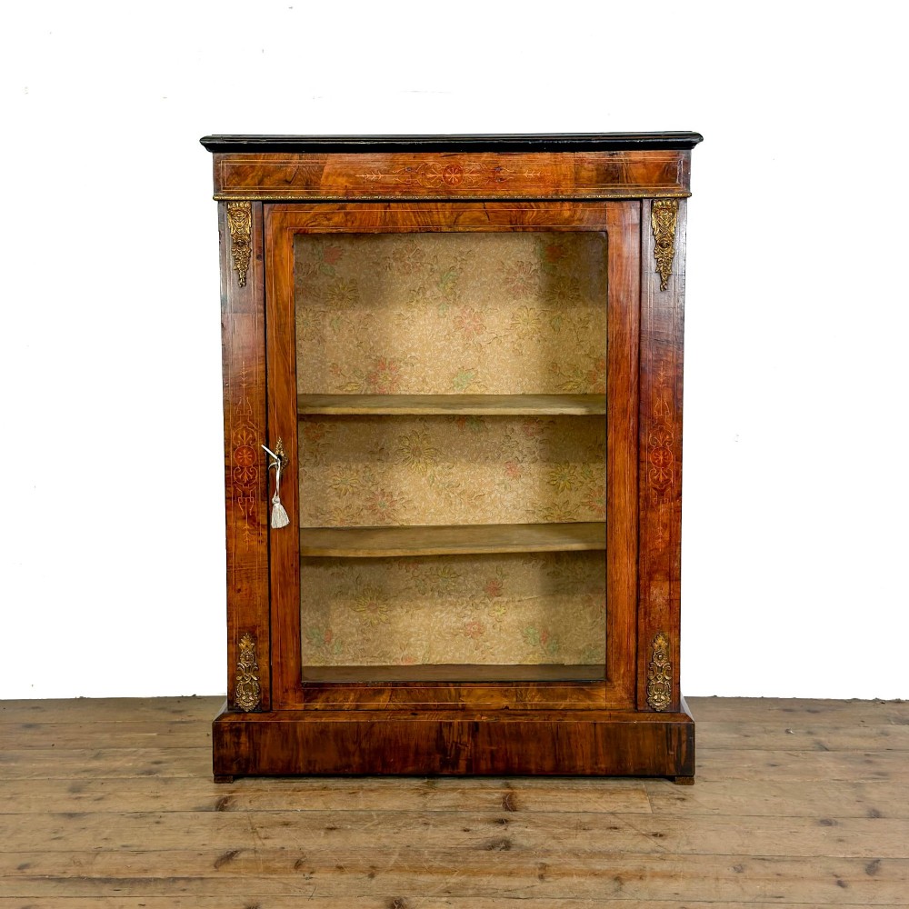 A Victorian inlaid walnut pier cabinet featuring a single glazed door, ormolu brass mounts, floral interior lining, and two interior shelves.