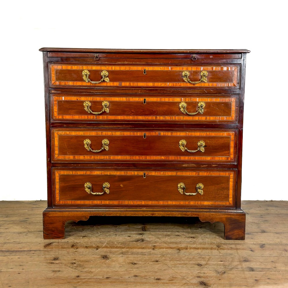 An antique mahogany bachelors chest featuring four crossbanded graduated drawers with brass handles, a brushing slide, and bracket feet.