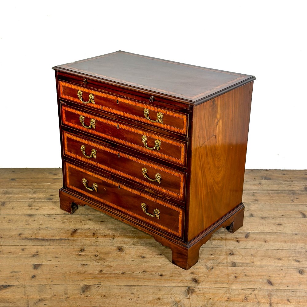 An antique mahogany bachelors chest featuring four crossbanded graduated drawers with brass handles, a brushing slide, and bracket feet. View III