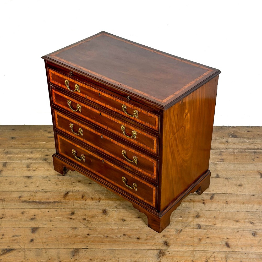 An antique mahogany bachelors chest featuring four crossbanded graduated drawers with brass handles, a brushing slide, and bracket feet. View IV