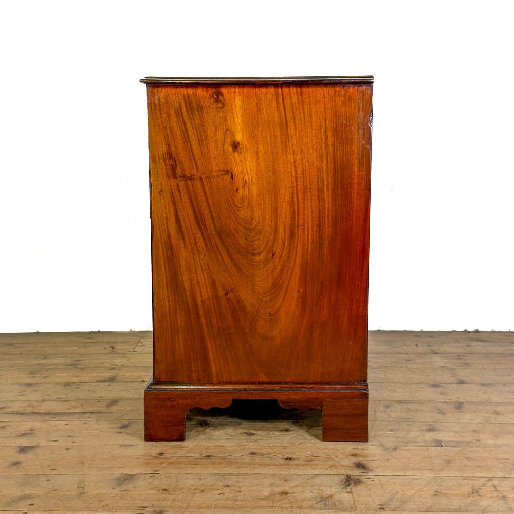 An antique mahogany bachelors chest featuring four crossbanded graduated drawers with brass handles, a brushing slide, and bracket feet. View V