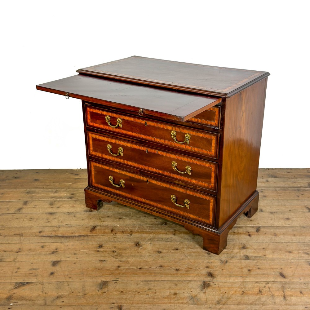 An antique mahogany bachelors chest featuring four crossbanded graduated drawers with brass handles, a brushing slide, and bracket feet. View IX