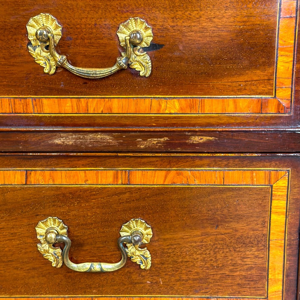 An antique mahogany bachelors chest featuring four crossbanded graduated drawers with brass handles, a brushing slide, and bracket feet. View X