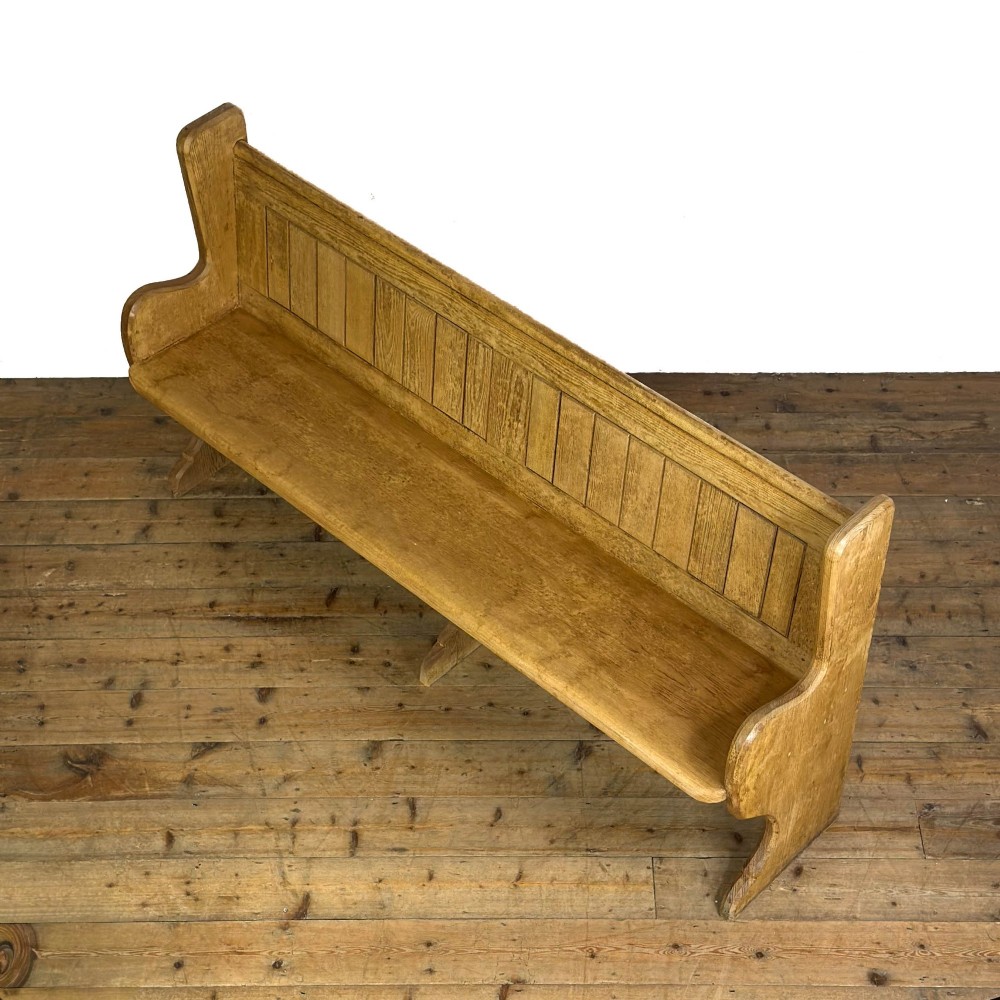 An antique pine chapel pew featuring a panelled backrest, integrated under-seat storage shelf, and sculpted bench ends. View III