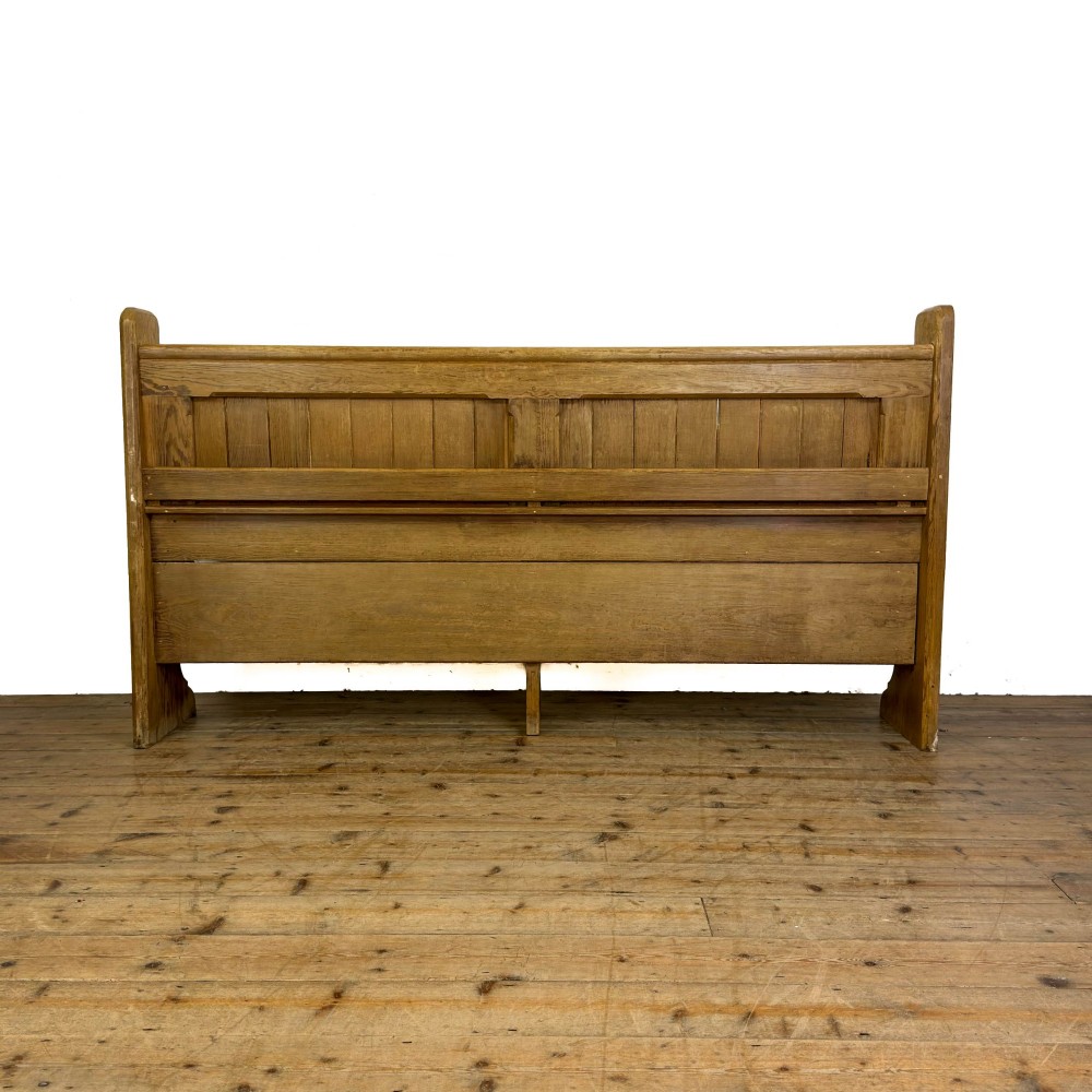 An antique pine chapel pew featuring a panelled backrest, integrated under-seat storage shelf, and sculpted bench ends. View VI