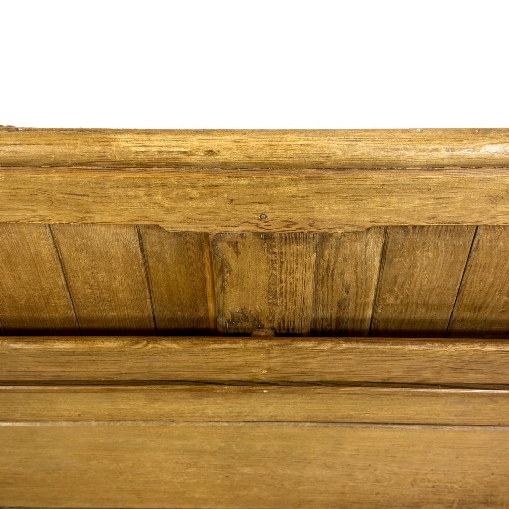An antique pine chapel pew featuring a panelled backrest, integrated under-seat storage shelf, and sculpted bench ends. View VII