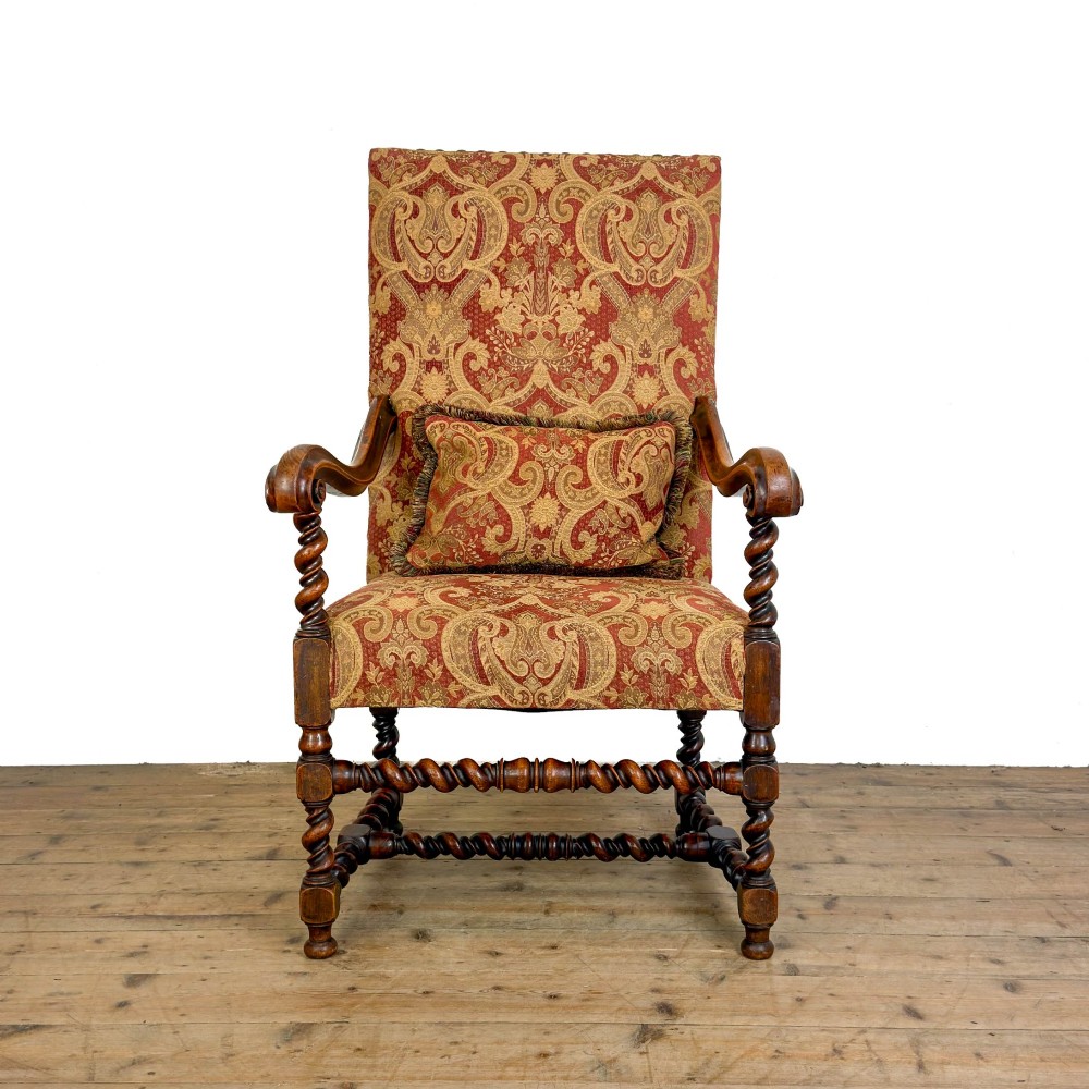 An antique walnut elbow chair featuring barley twist turnings, scrolled arms, and red and gold patterned upholstery with a matching cushion.