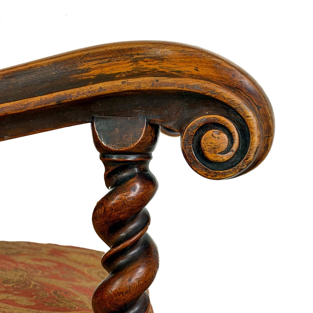 An antique walnut elbow chair featuring barley twist turnings, scrolled arms, and red and gold patterned upholstery with a matching cushion. View V