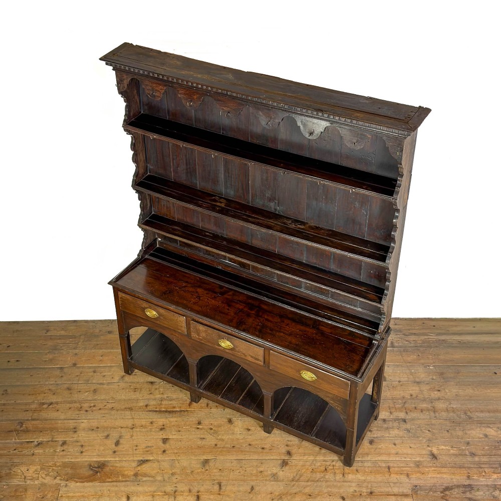 A dark oak 19th-century Welsh dresser featuring a three-tier open plate rack with a scalloped canopy above three drawers and an open pot board lower section. View II