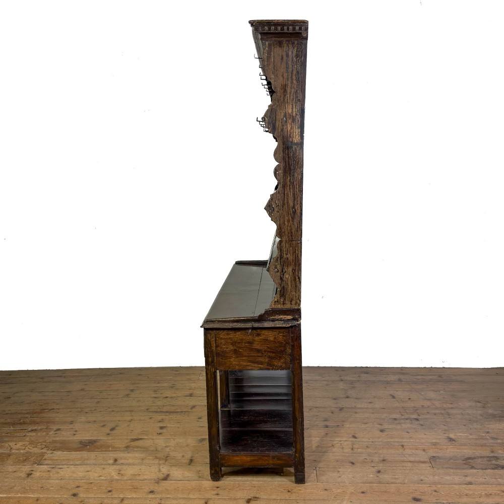 A dark oak 19th-century Welsh dresser featuring a three-tier open plate rack with a scalloped canopy above three drawers and an open pot board lower section. View IV