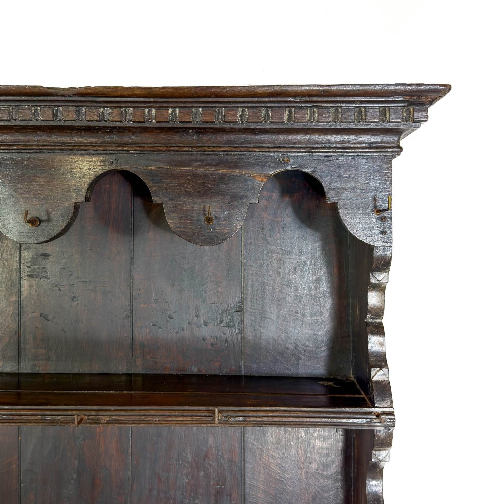 A dark oak 19th-century Welsh dresser featuring a three-tier open plate rack with a scalloped canopy above three drawers and an open pot board lower section. View VII