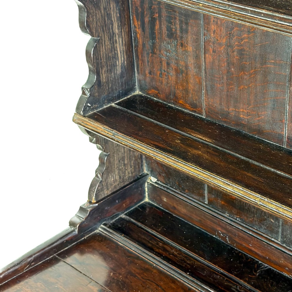 A dark oak 19th-century Welsh dresser featuring a three-tier open plate rack with a scalloped canopy above three drawers and an open pot board lower section. View X