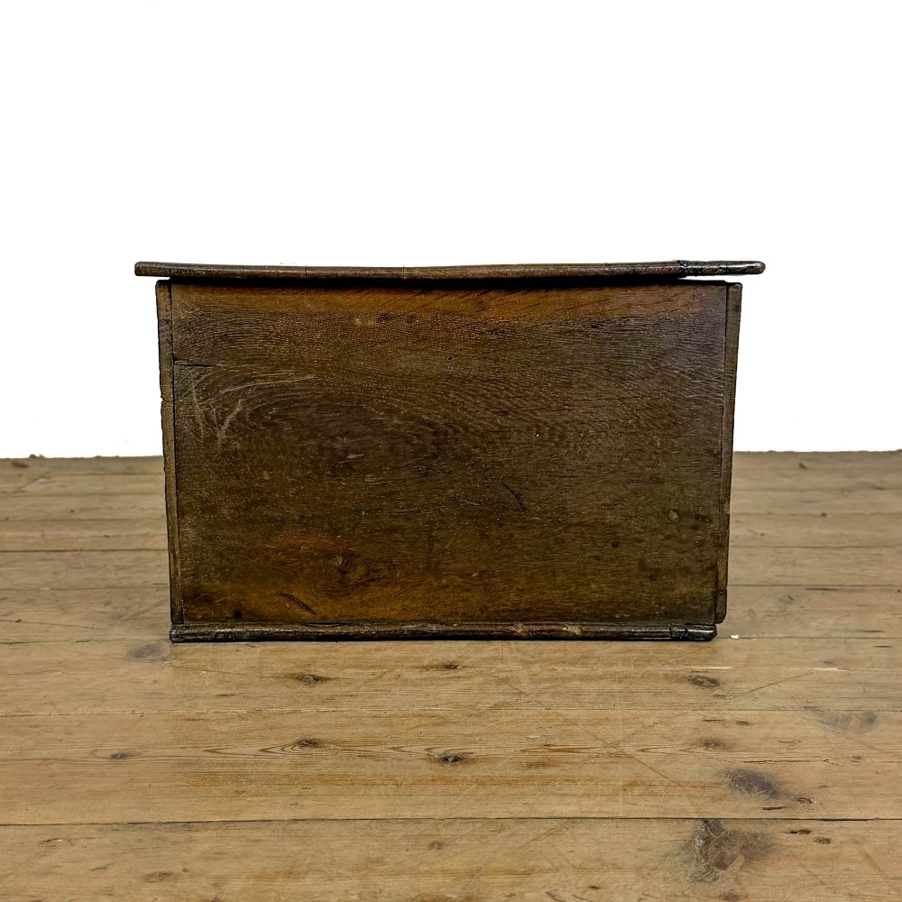 An 18th-century dark oak bible box featuring a hinged top lid, carved initials flanking a central iron lock plate, and a rectangular timber body. View VI