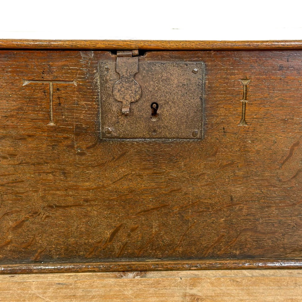 An 18th-century dark oak bible box featuring a hinged top lid, carved initials flanking a central iron lock plate, and a rectangular timber body. View VII
