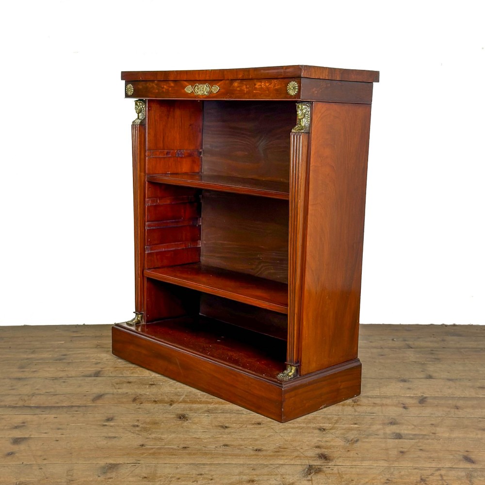 An antique Egyptian Revival mahogany open bookcase featuring fluted pilasters topped with cast brass sphinx heads, adjustable wooden shelves, and a plinth base. View VI