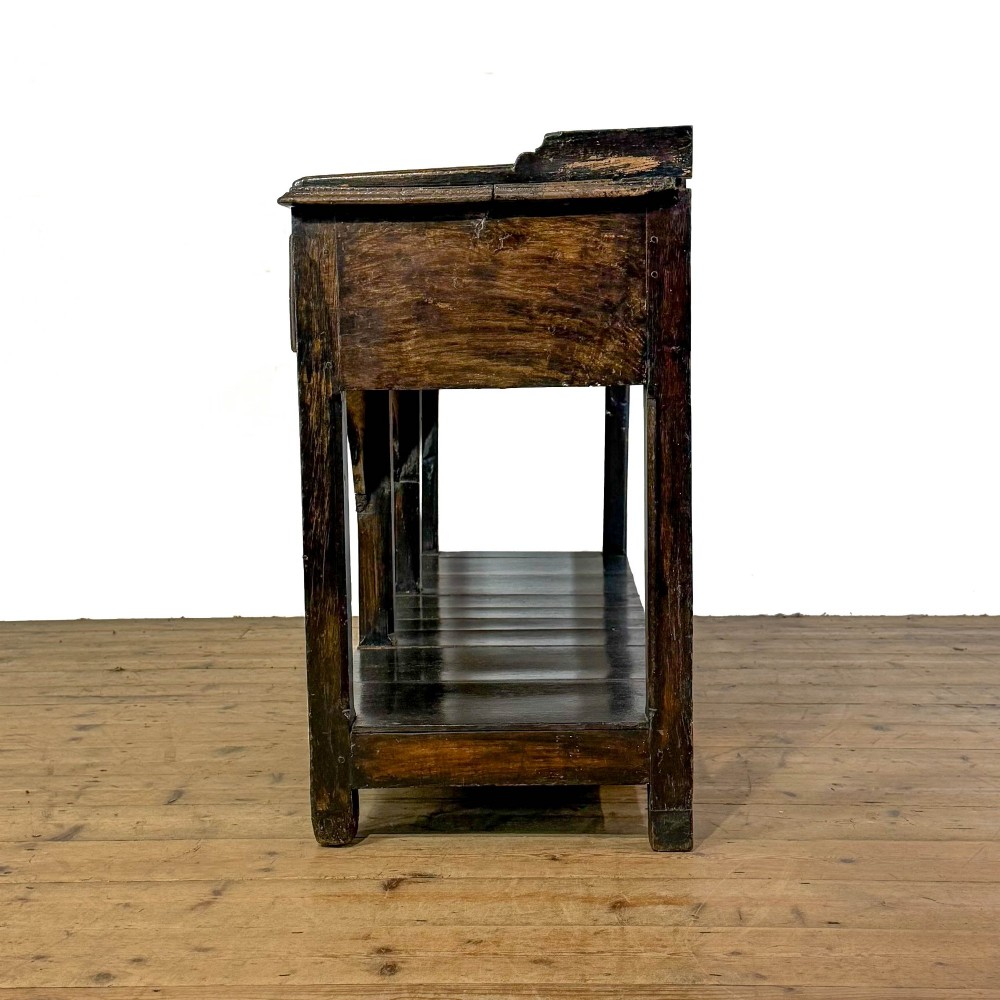 A 19th-century dark oak dresser base featuring three upper drawers with brass oval handles, three decorative arched aprons, and a low potboard shelf. View II