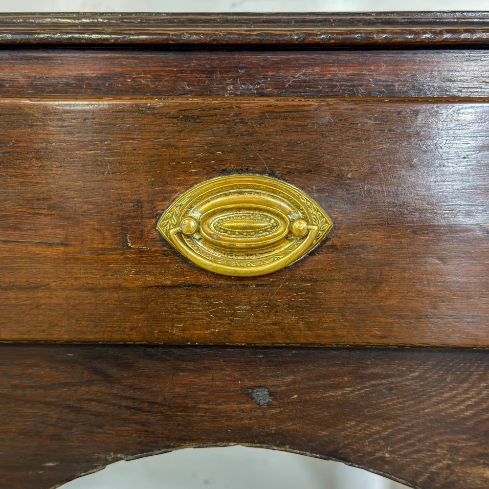 A 19th-century dark oak dresser base featuring three upper drawers with brass oval handles, three decorative arched aprons, and a low potboard shelf. View VI