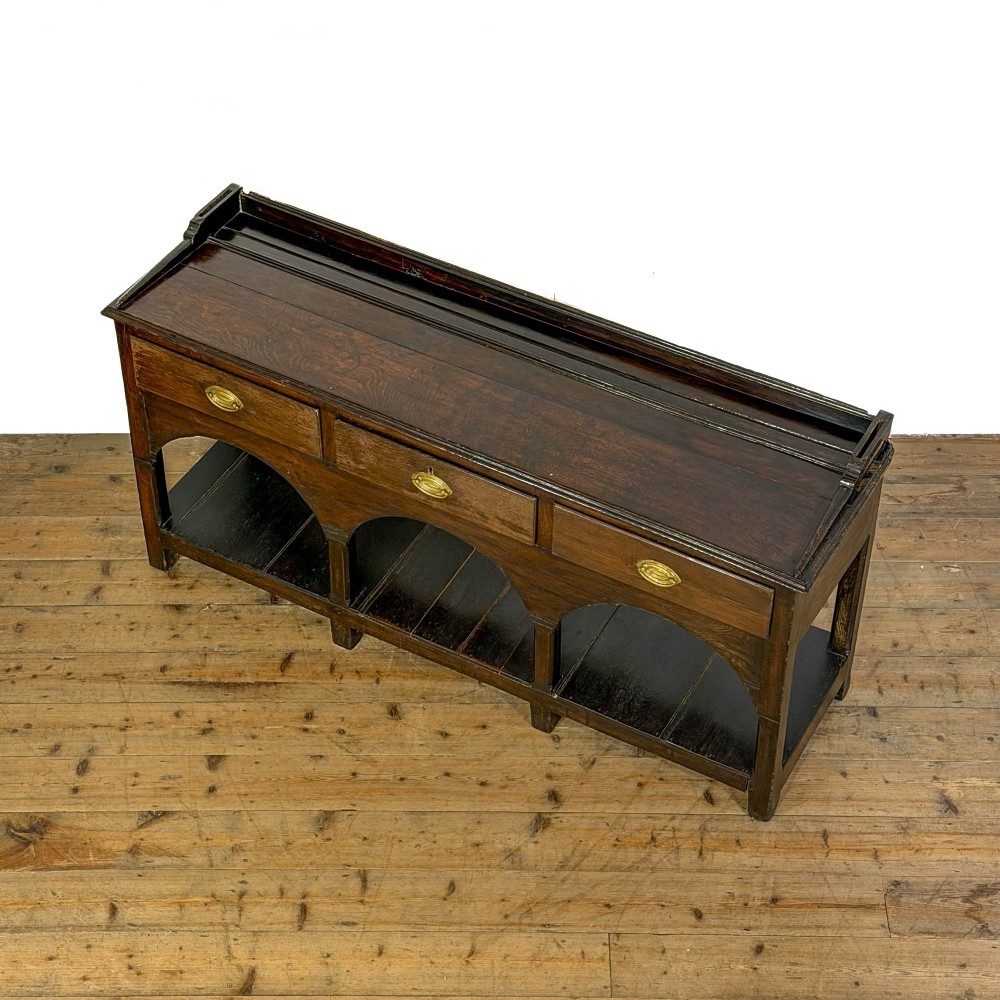 A 19th-century dark oak dresser base featuring three upper drawers with brass oval handles, three decorative arched aprons, and a low potboard shelf. View VIII
