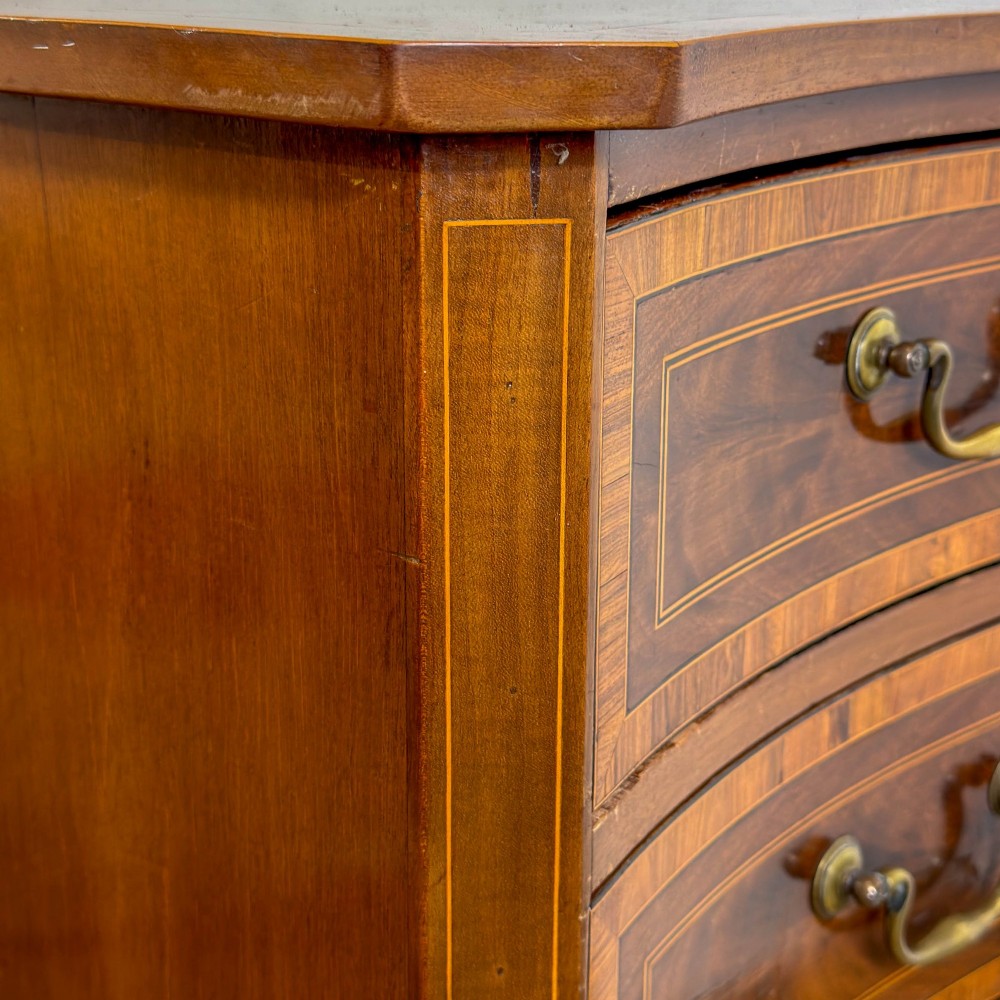 An antique mahogany serpentine chest featuring five graduated drawers with brass swan-neck handles and crossbanded inlay. View VI