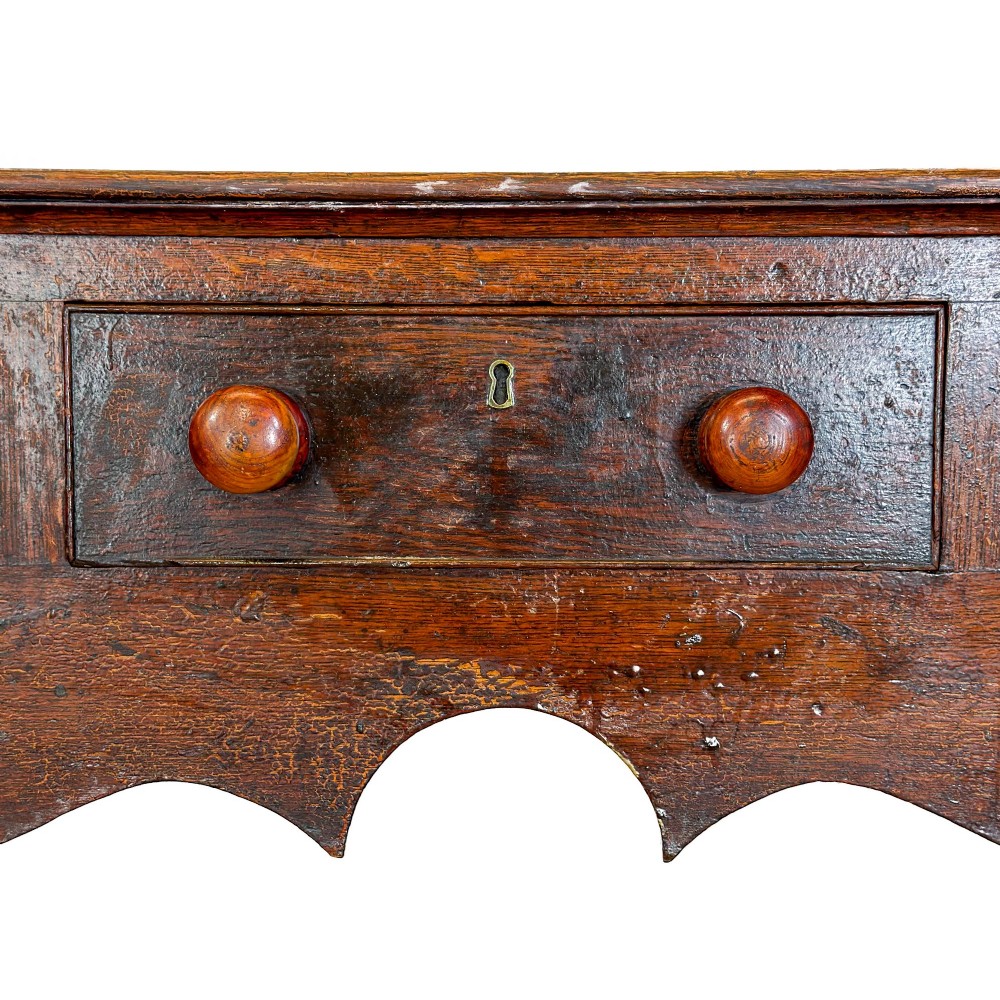 An antique dark wood dresser base featuring turned front legs, a scalloped apron, multiple drawers with wooden knob handles, and a lower pot board shelf. View II