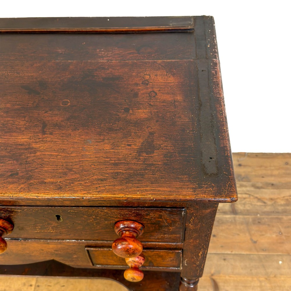 An antique dark wood dresser base featuring turned front legs, a scalloped apron, multiple drawers with wooden knob handles, and a lower pot board shelf. View III