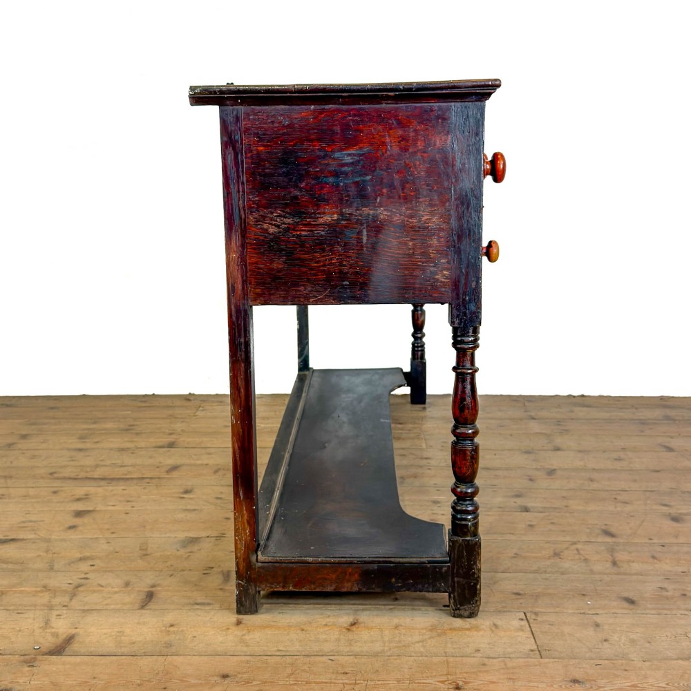 An antique dark wood dresser base featuring turned front legs, a scalloped apron, multiple drawers with wooden knob handles, and a lower pot board shelf. View IV