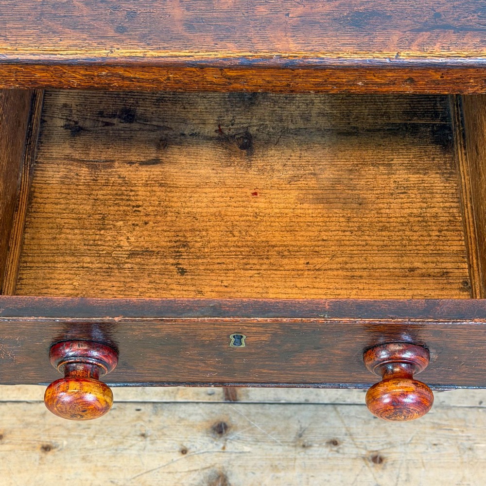 An antique dark wood dresser base featuring turned front legs, a scalloped apron, multiple drawers with wooden knob handles, and a lower pot board shelf. View V