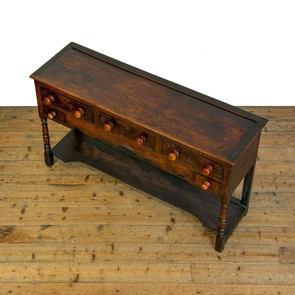 An antique dark wood dresser base featuring turned front legs, a scalloped apron, multiple drawers with wooden knob handles, and a lower pot board shelf. View VI