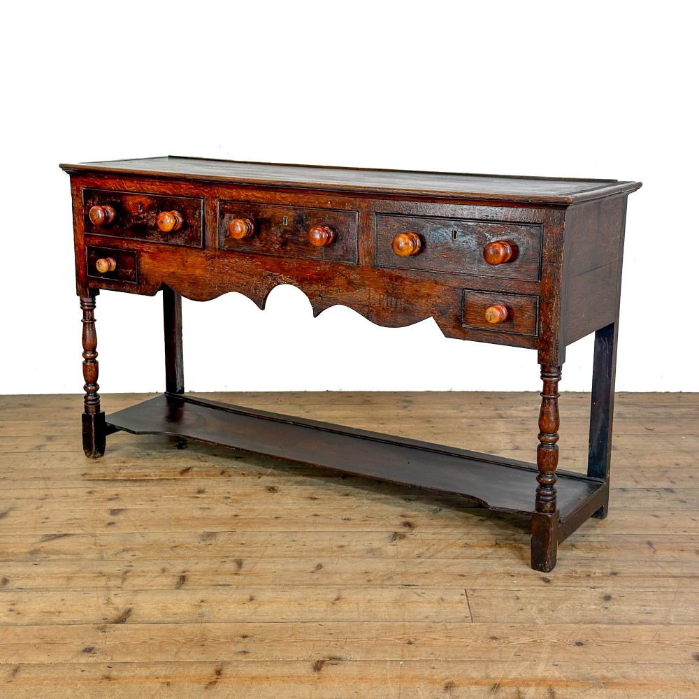 An antique dark wood dresser base featuring turned front legs, a scalloped apron, multiple drawers with wooden knob handles, and a lower pot board shelf. View VII