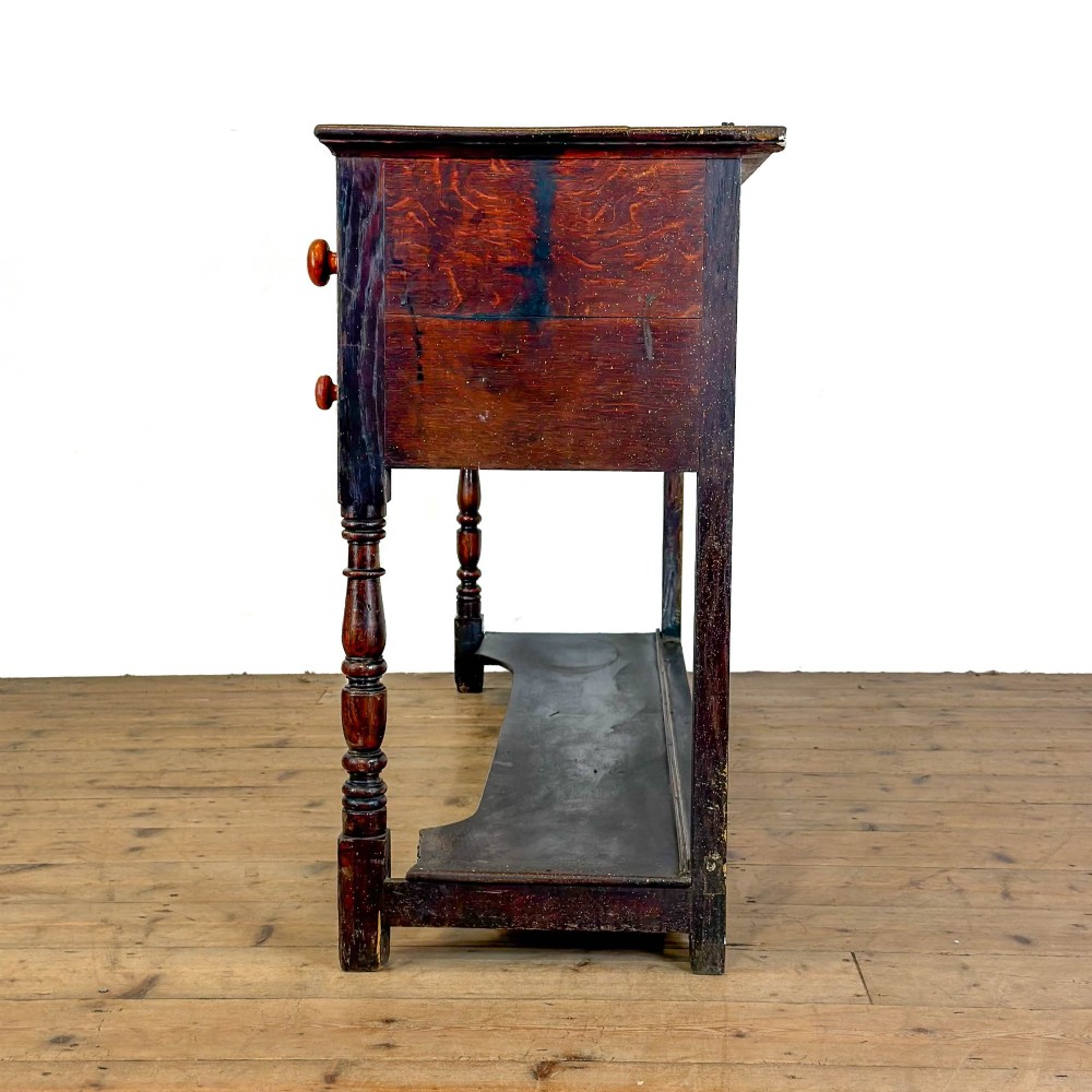 An antique dark wood dresser base featuring turned front legs, a scalloped apron, multiple drawers with wooden knob handles, and a lower pot board shelf. View VIII