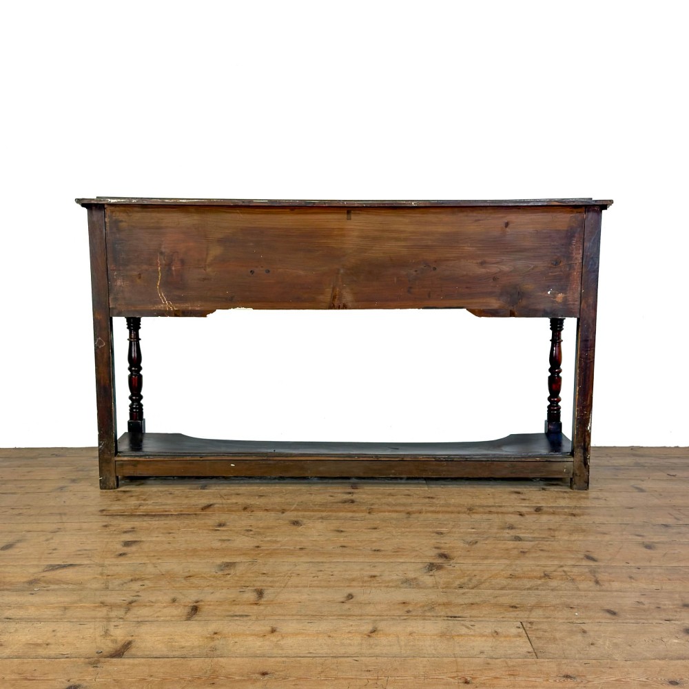 An antique dark wood dresser base featuring turned front legs, a scalloped apron, multiple drawers with wooden knob handles, and a lower pot board shelf. View X