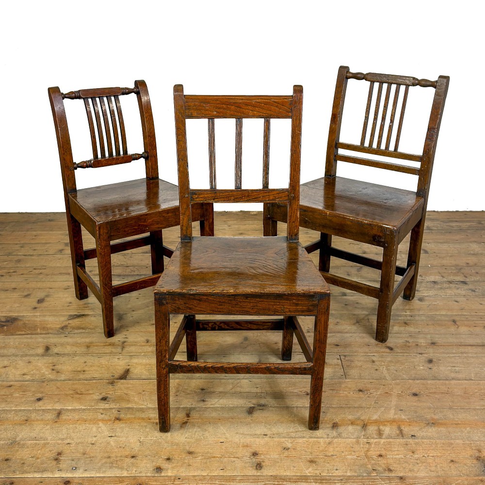A set of three dark oak farmhouse dining chairs featuring vertical slat backs, solid wooden seats, and sturdy square stretchers.