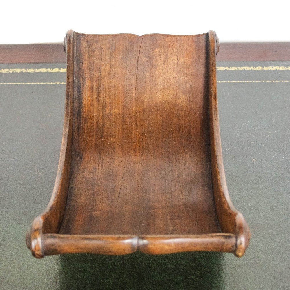 A Georgian mahogany cheese coaster featuring a curved trough with turned scroll ends resting on a rectangular base. View VI