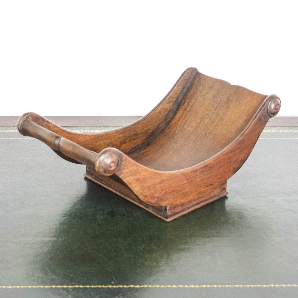 A Georgian mahogany cheese coaster featuring a curved trough with turned scroll ends resting on a rectangular base. View VII