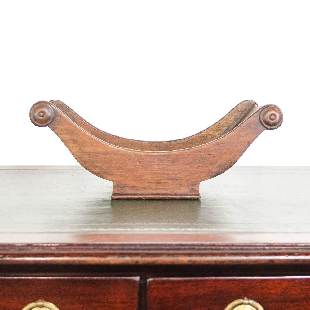 A Georgian mahogany cheese coaster featuring a curved trough with turned scroll ends resting on a rectangular base. View IX