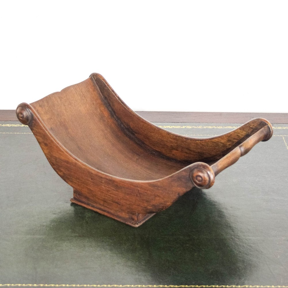 A Georgian mahogany cheese coaster featuring a curved trough with turned scroll ends resting on a rectangular base. View X